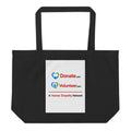 A black canvas tote bag with two shoulder straps, featuring a white rectangular printed panel on the front with the Donate.com and Volunteer.com logos and A Human Empathy Network description