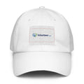 A white baseball cap featuring a rectangular embroidered patch on the front with the Volunteer.com logo in blue and green, outlined with a thin red border, set against a plain white background.